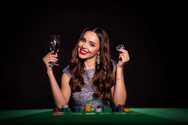 Foto van charmante gelukkige mooie vrouw zitten pokertafel houden poker chips champagne geïsoleerd op zwarte kleur achtergrond — Stockfoto