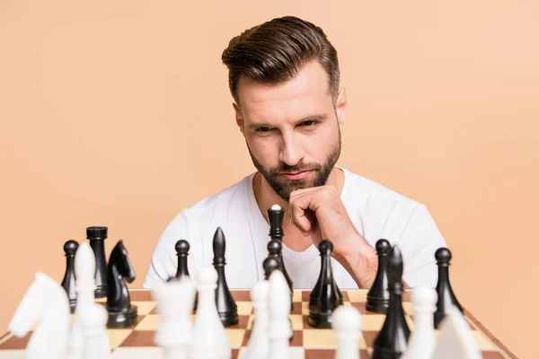 Портрет милого парня, играющего в шахматы, думающего слишком много, решившего сделать следующий шаг изолированным на бежевом пастельном фоне. — стоковое фото