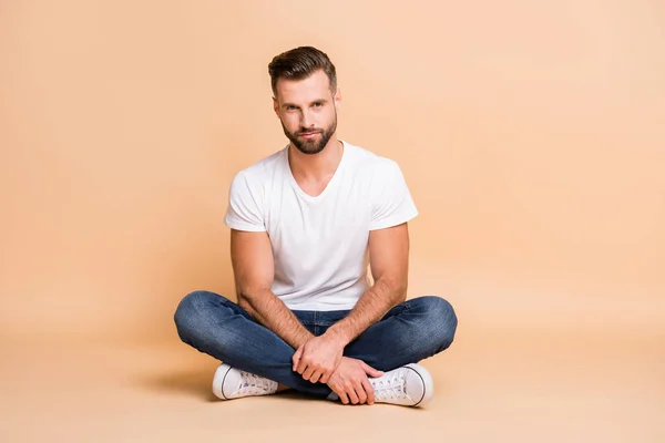 Retrato de macho atractivo tipo en forma sentada en el suelo en pose de loto con ropa acogedora aislada sobre fondo de color beige —  Fotos de Stock