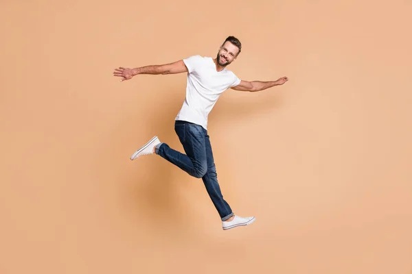 Взгляд в полный рост на симпатичного веселого парня, прыгающего с хорошим настроением на бежевом фоне — стоковое фото