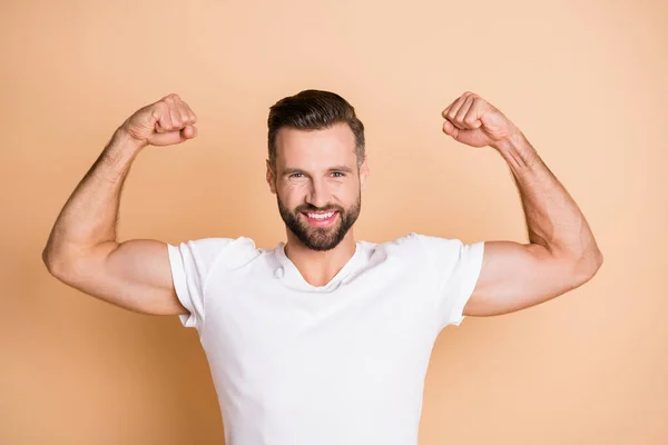 Portret van aantrekkelijke vrolijke jongen tonen spieren kampioen concurrent geïsoleerd over beige pastel kleur achtergrond — Stockfoto