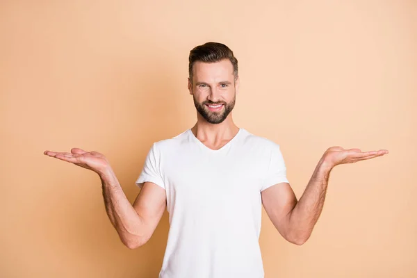 Foto di giovane bell'uomo felice sorriso positivo tenere due mani equilibrio confrontare offerta di prodotto isolato su sfondo di colore beige — Foto Stock