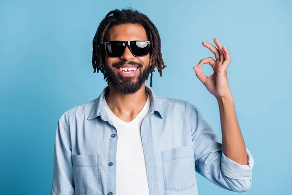 Portrett av munter, kjekk, mørk hud Han som stråler smil fingre viser okey symbol isolert på blå bakgrunn – stockfoto