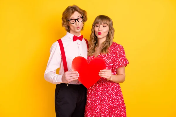Photo portrait of beloved couple sending air kiss showing red heart on valentines day isolated on vibrant yellow background — Stock Photo, Image