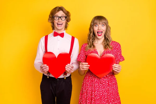 Photo portrait of amazed boyfriend girlfriend keeping red hearts love symbols on date isolated on vibrant yellow background — Stock Photo, Image