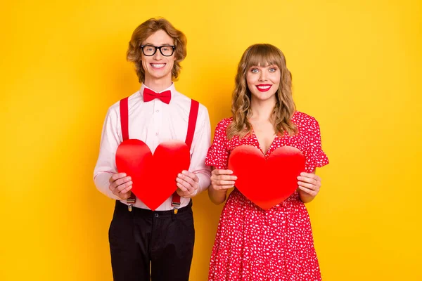 Foto retrato de menino e menina mantendo cartões postais em forma de coração vermelho na data isolada no fundo amarelo vibrante — Fotografia de Stock