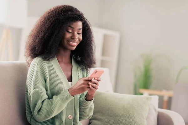 Foto de joven atractiva mujer negra feliz sonrisa positiva leer navegar teléfono celular chat tipo sms sentarse sofá en casa — Foto de Stock