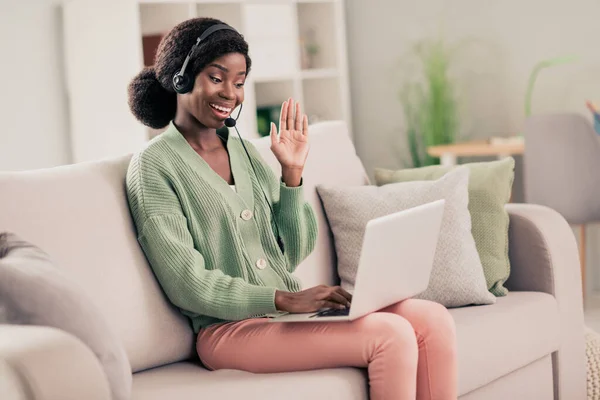 Retrato de chica alegre atractiva sentada en diván usando el ordenador portátil saludando a la reunión de asistencia en casa plana sala de estar interior — Foto de Stock