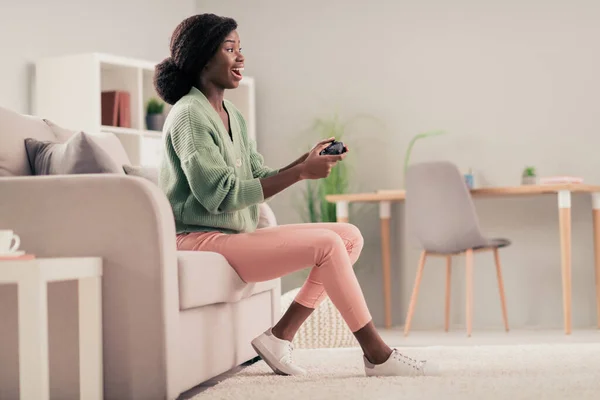 Cuerpo completo tamaño foto chica jugando videojuegos mantener joystick riendo sentado en el sofá — Foto de Stock