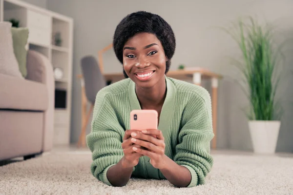 Foto de la joven atractiva mujer africana feliz sonrisa positiva leer navegar por el teléfono celular yacía en el interior — Foto de Stock