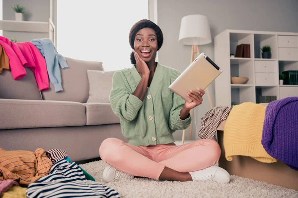 Foto de longitud completa de la joven chica negra feliz sonrisa positiva hacer compras en línea comprar indican elección de ropa de dedo sentarse piso en el interior — Foto de Stock