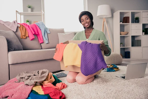 Retrato de chica alegre atractiva sentada en el piso plegable de la ropa que se reúne en las tareas de la economía de la caja en la casa plana sala de estar interior —  Fotos de Stock