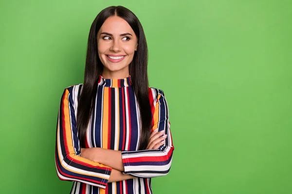 Foto van optimistische brunette dame gekruiste armen kijken lege ruimte dragen kleurrijke gestreepte shirt geïsoleerd op groene kleur achtergrond — Stockfoto