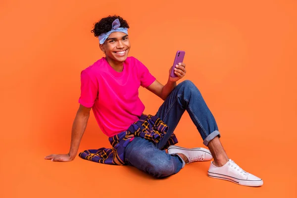 Volledige lichaamslengte foto van gelukkige jongeman zitten met behulp van mobiele telefoon app surfen internet geïsoleerde levendige oranje kleur achtergrond — Stockfoto