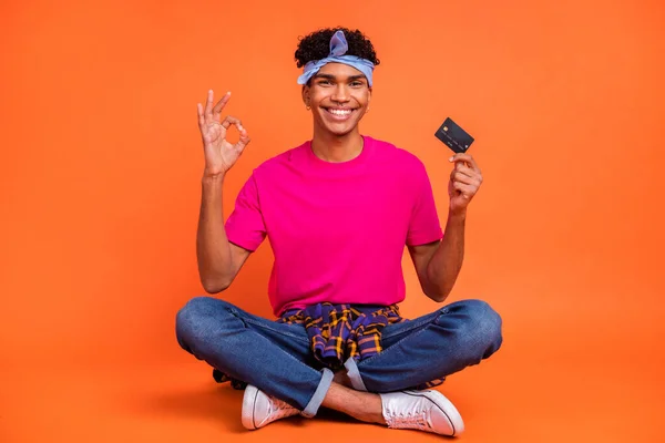 Lunghezza totale dimensioni del corpo foto di giovane hipster mostrando carta di credito ok gesto dita isolate su sfondo di colore arancione vivido — Foto Stock