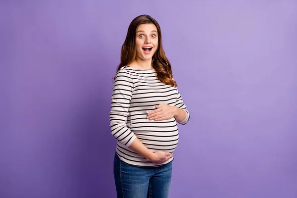 Foto von glänzend beeindruckt Frau erwartet Kind tragen gestreifte Hemd umarmt Bauch isoliert lila Farbe Hintergrund — Stockfoto