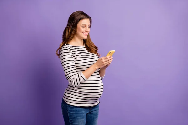 Foto retrato de mulher grávida segurando telefone em duas mãos isoladas em fundo colorido violeta vívido — Fotografia de Stock
