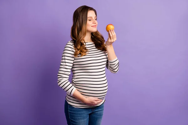 Foto de señora bastante soñadora esperando bebé vestido camisa a rayas brazo vientre disfrutar de fruta aroma aislado color violeta fondo — Foto de Stock