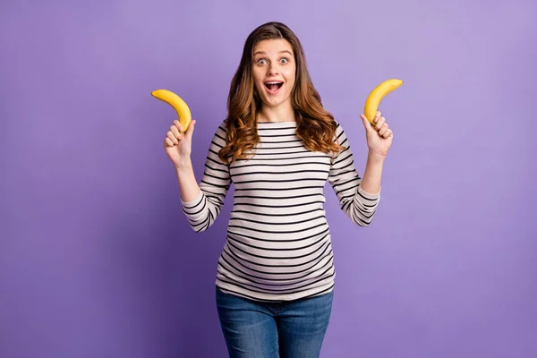 Φωτογραφία πορτρέτο της εγκύου ενθουσιασμένοι γυναίκα κρατώντας δύο μπανάνες απομονώνονται σε ζωντανό βιολετί χρώμα φόντο — Φωτογραφία Αρχείου