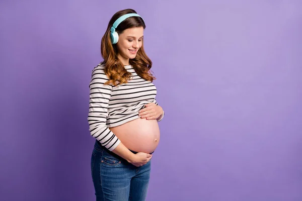 Foto van dromerige dame wachtend baby gekleed gestreepte shirt armen buik luisteren muziek lege ruimte geïsoleerde violette kleur achtergrond — Stockfoto