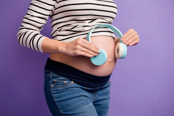 Foto recortada de fones de ouvido senhora grávida abdômen nu usar camisa listrada isolado cor roxa fundo — Fotografia de Stock