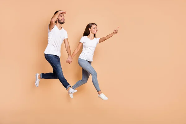 Foto de comprimento total do jovem casal feliz sorriso salto ir menina ponto dedo vazio espaço cara olhar para a frente isolado sobre cor bege fundo — Fotografia de Stock