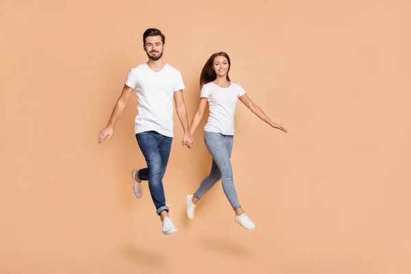 Foto de larga duración de la joven pareja alegre feliz sonrisa positiva salto ir caminar correr tomar de las manos aisladas sobre fondo de color beige —  Fotos de Stock