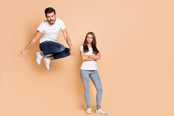 Corpo inteiro foto de jovem casal ele feliz se divertir saltar para cima ela olhar irritado triste cruzado mãos isolado sobre cor bege fundo — Fotografia de Stock