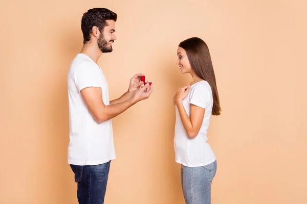 Foto de encantadora pareja adorable vestida con camisetas blancas haciendo propuesta caja de anillo rojo aislado color beige fondo —  Fotos de Stock