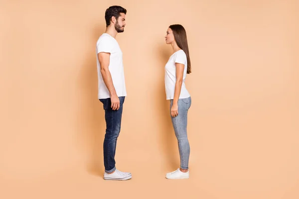Фотографія повної довжини одруженої пари одягнених білих футболок джинсових кросівок, які дивляться один на одного ізольованого бежевого кольору фону — стокове фото