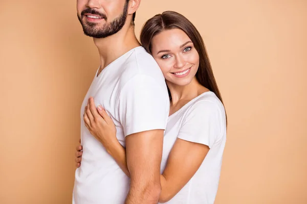 Photo recadrée de charmant couple marié brillant habillé de t-shirts blancs étreignant arrière-plan de couleur beige isolé souriant — Photo