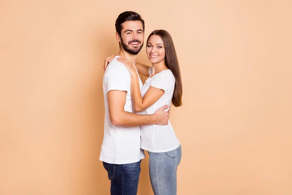 Foto de bonito bonito marido esposa desgaste branco t-shirts abraçando sorrindo isolado cor bege fundo — Fotografia de Stock