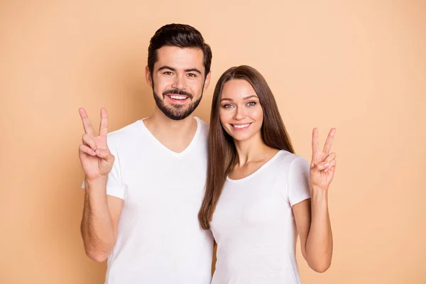 Foto de marido bastante dulce esposa usar camisetas blancas abrazos mostrando v-signo aislado color beige fondo — Foto de Stock