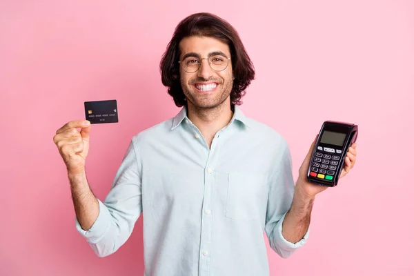 Portret van jonge knappe glimlachende vrolijke man man man houden credit card terminal slijtage bril geïsoleerd op roze kleur achtergrond — Stockfoto