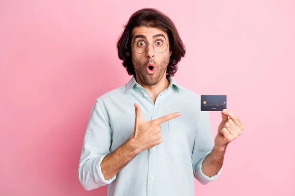 Foto de impresionado pelo castaño asombrado chico punto tarjeta desgaste gafas camisa azul aislado sobre fondo de color rosa pastel — Foto de Stock