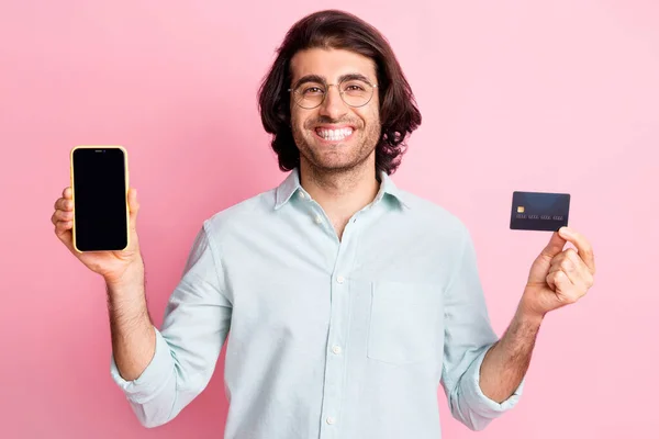 Foto van vrolijke goed uitziende bruine haar man show telefoonkaart dragen bril blauw shirt geïsoleerd op pastel roze kleur achtergrond — Stockfoto