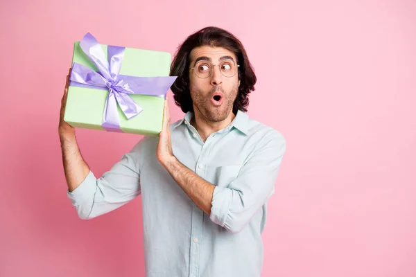 Фото впечатлен смешной каштановые волосы парень держать подарок носить очки рубашку изолированы на пастельно-розовый цвет фона — стоковое фото