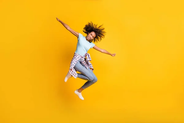 Full length photo of funny sweet dark skin wavy lady wear blue t-shirt jumping high empty space isolated yellow color background