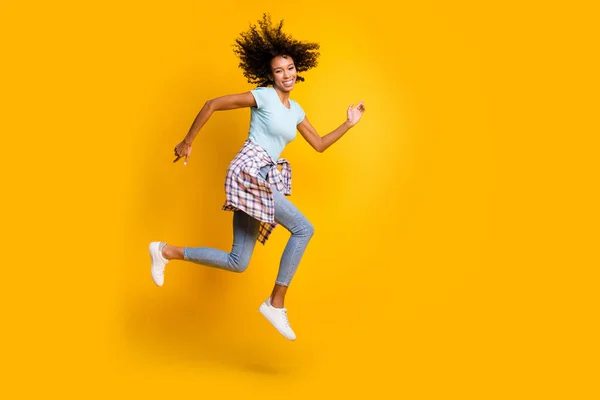 Foto de dulce encantadora mujer de piel oscura rizada vestida camiseta azul saltando corriendo rápido aislado color amarillo fondo —  Fotos de Stock