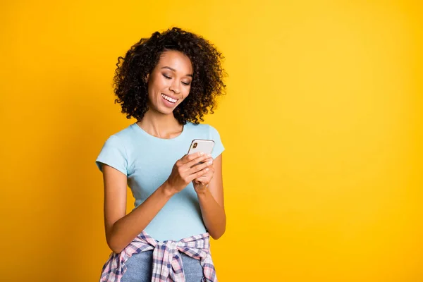 Foto van vrolijke zoete donkere huid golvende dame dragen blauwe t-shirt met moderne gadget lege ruimte geïsoleerde gele kleur achtergrond — Stockfoto