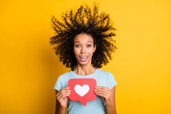 Foto de divertida linda piel oscura dama ondulada desgaste azul camiseta soplado de aire sosteniendo rojo como signo aislado color amarillo fondo —  Fotos de Stock