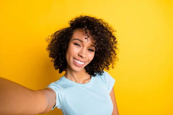 Foto de divertida encantadora chica rizada de piel oscura vestida con camiseta azul haciendo selfie aislado color amarillo fondo —  Fotos de Stock