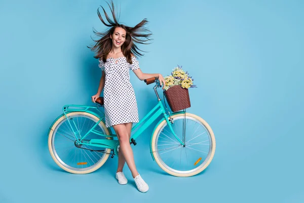 Foto de comprimento total da menina bicicleta flor cesta vento sopro cabelo desgaste pontilhado vestido curto calçado isolado azul cor fundo — Fotografia de Stock