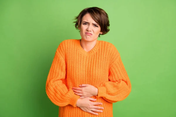 Retrato de mujer morena triste dolor de estómago usar suéter naranja aislado sobre fondo verde pastel — Foto de Stock