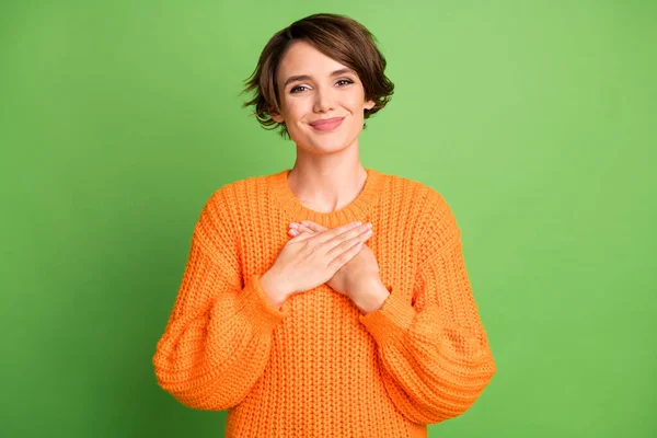 楽観的なブルネットの女性の手の胸はパステルグリーンの背景に隔離されたオレンジ色のセーターを着用 — ストック写真