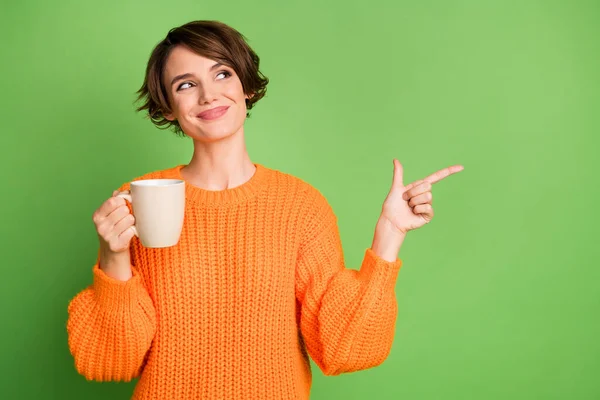 Fotografie šťastné trendy mladá žena vzhled bod ukazováček prázdný prostor držet hrnek káva izolované na zeleném pozadí — Stock fotografie
