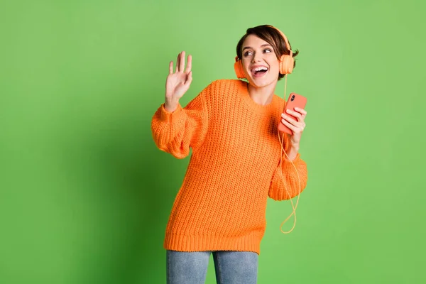 Foto de funky feliz joven mujer mantenga teléfono inteligente buen humor desgaste auriculares mirada espacio vacío aislado sobre fondo de color verde — Foto de Stock