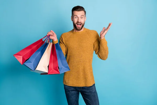 Porträt der attraktiven erstaunt fröhlichen Kerl hält in den Händen stapeln Taschen Dinge Spaß isoliert über hellblauen Farbhintergrund — Stockfoto