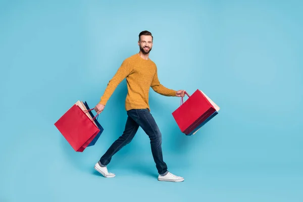 Повний розмір профілю фотографія молодого щасливого позитивного веселого чоловіка йти пішки з сумками ізольовані на синьому кольоровому фоні — стокове фото
