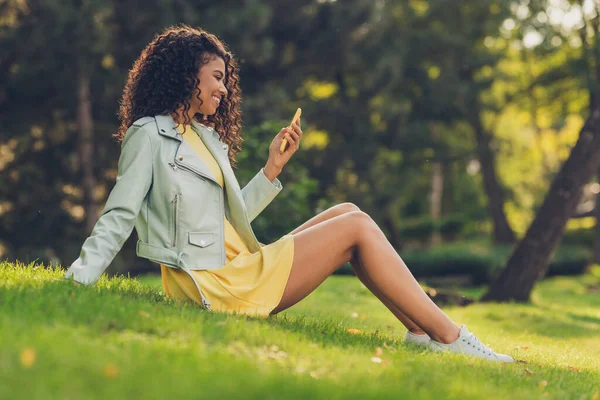 Perfil vista lateral retrato de menina alegre atraente sentado na grama usando o aplicativo do dispositivo 5g navegação na web passar tempo livre no parque ao ar livre — Fotografia de Stock